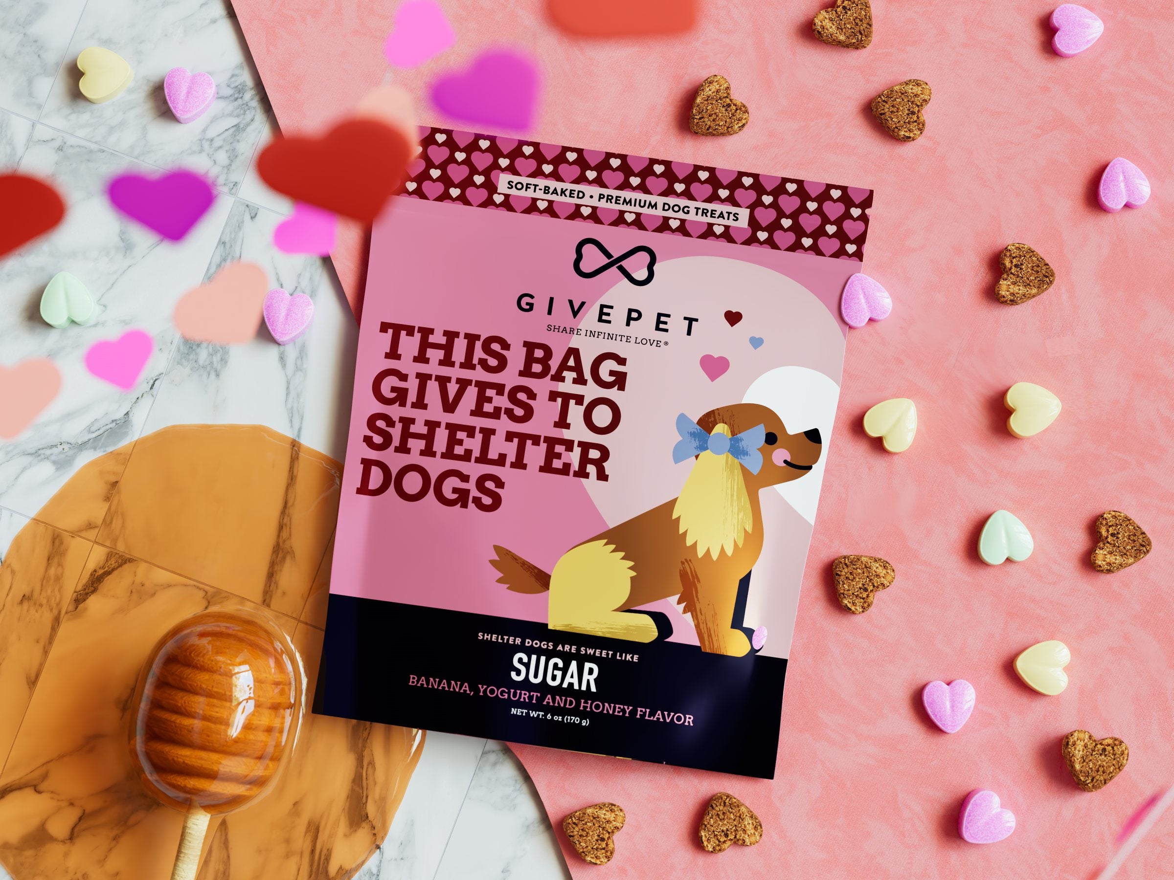 Sugar pouch on a pink marble table among candy hearts, treats and a honey dipper